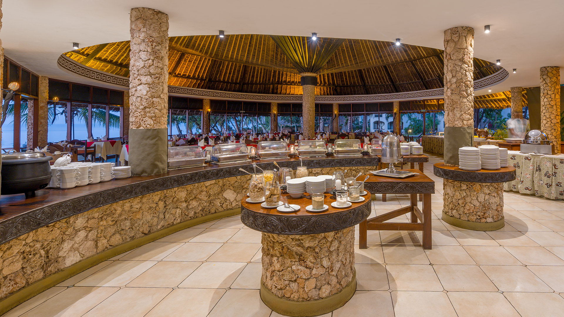 Buffet dining pavilion with coral-stone pillars and ocean view at twilight