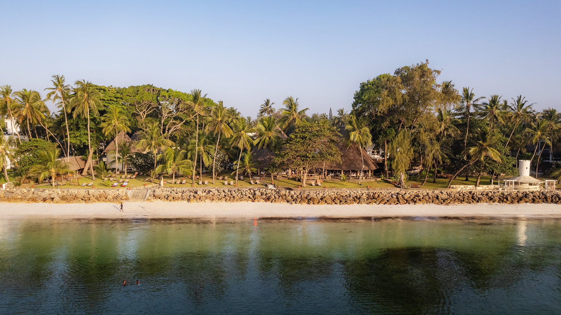 Aerial view of Bamburi Beach with turquoise water, white sand, and palm-shaded resort lawns