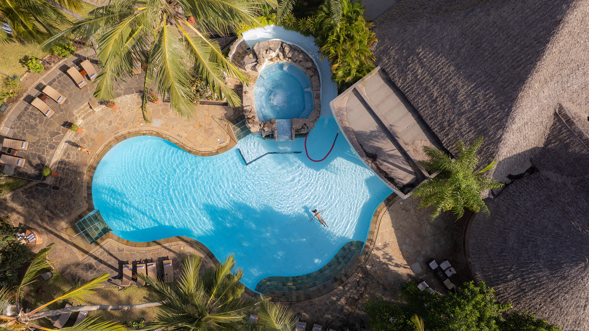Aerial view of a tropical resort swimming pool with lounge chairs and thatched roofs