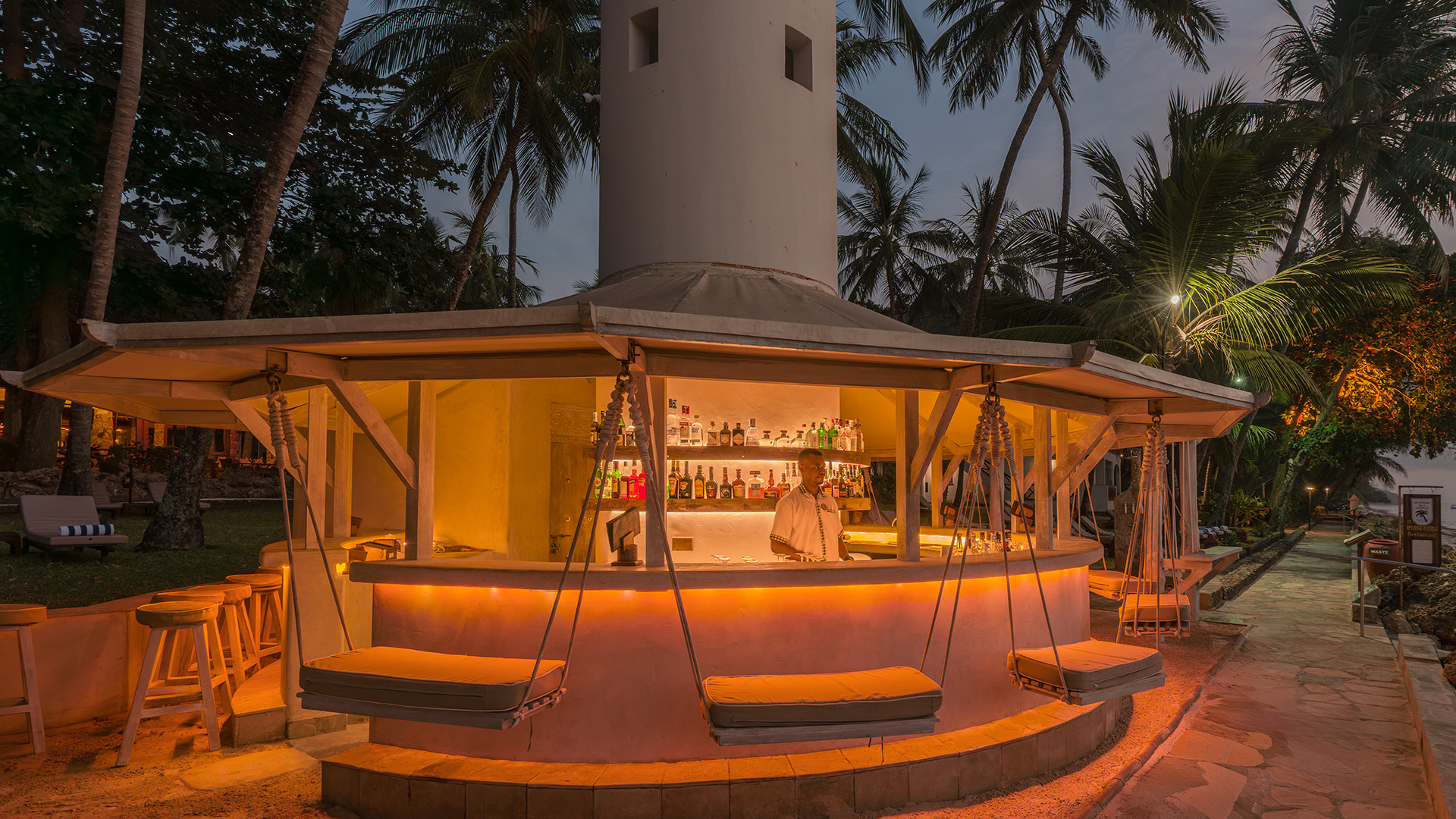 Circular beach bar with hanging swing seats and lighthouse tower at twilight
