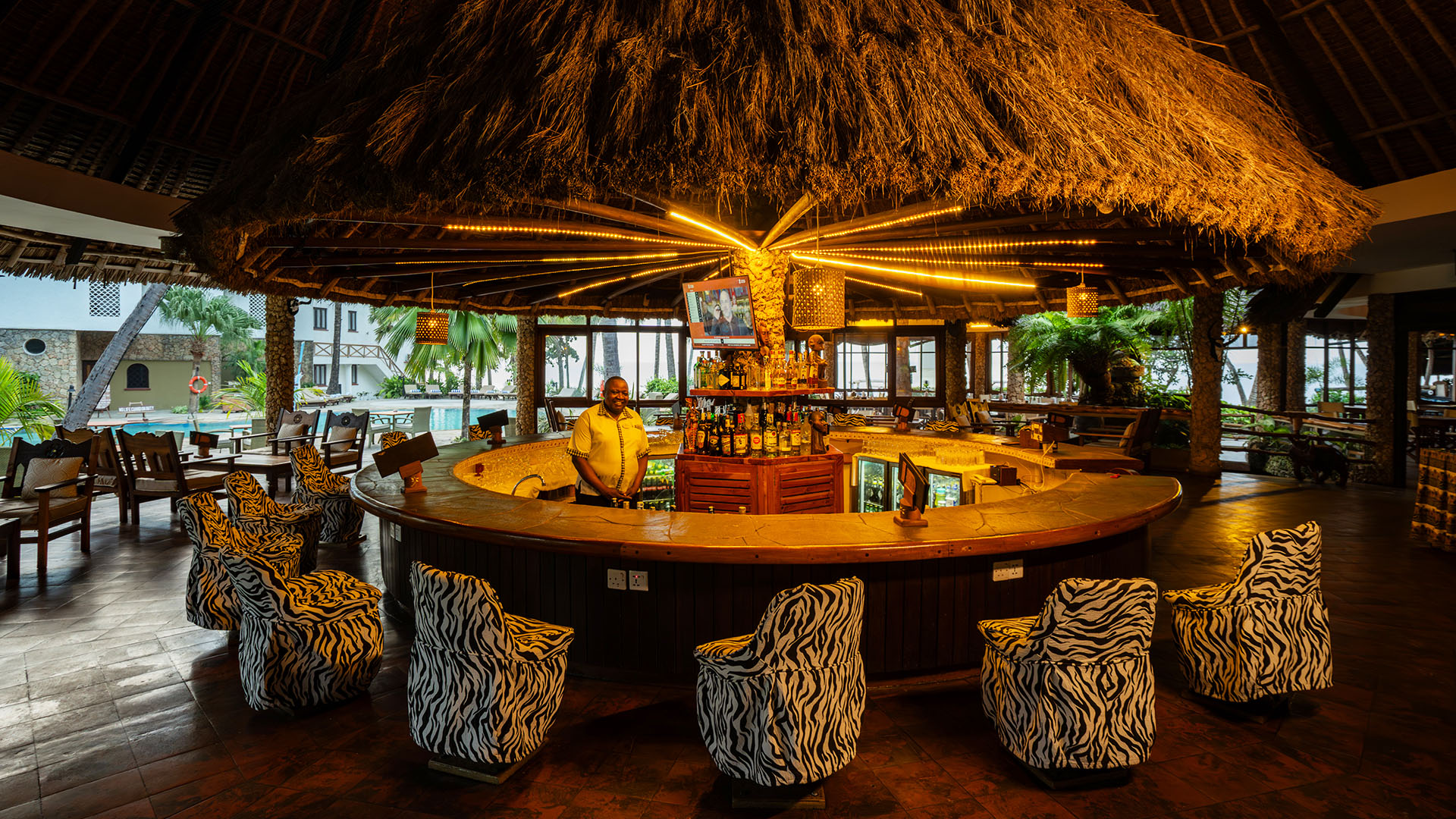 Circular thatched bar with zebra-print chairs overlooking the resort pool