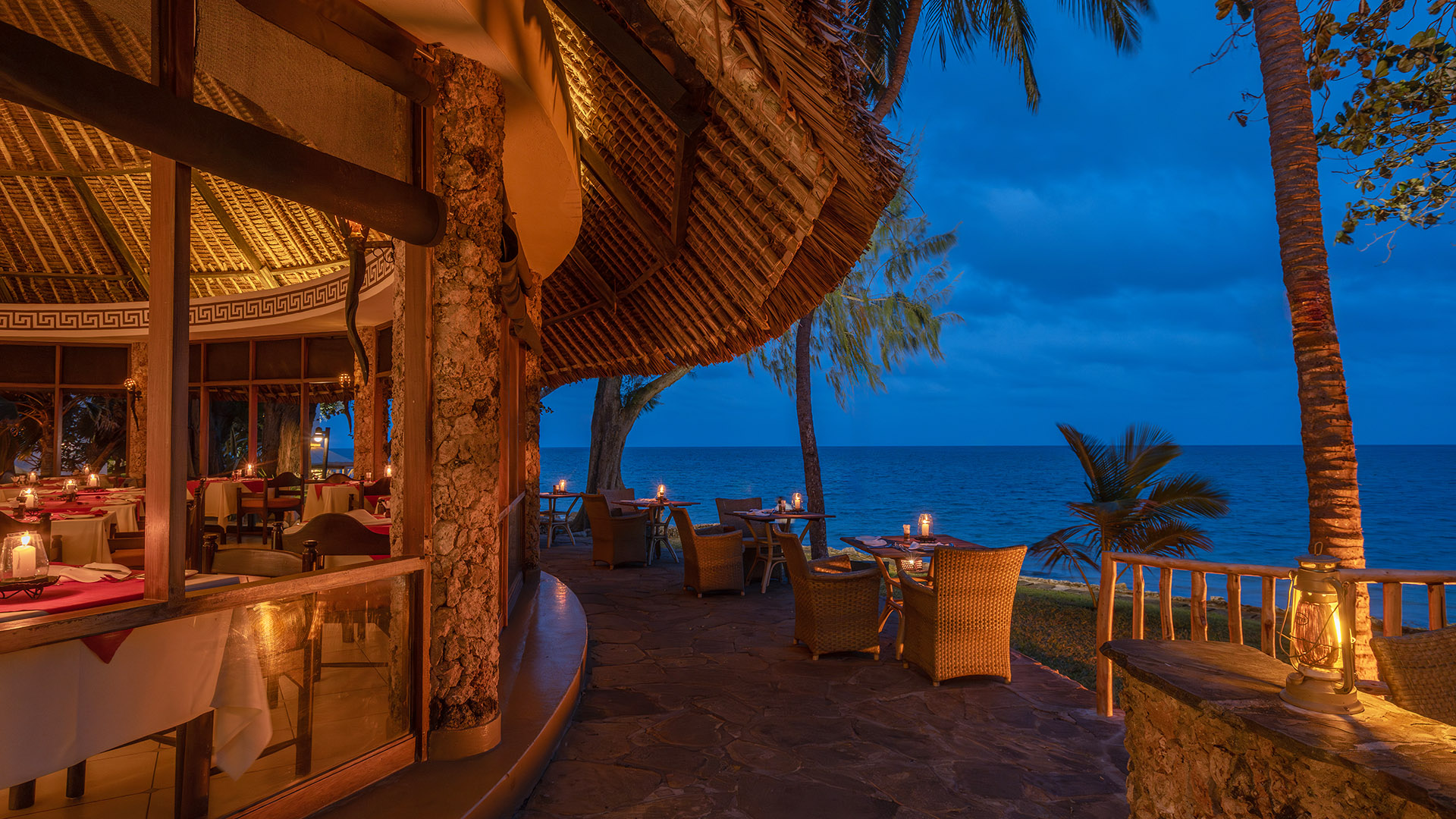 Seaside restaurant patio with candlelit tables overlooking the ocean at dusk