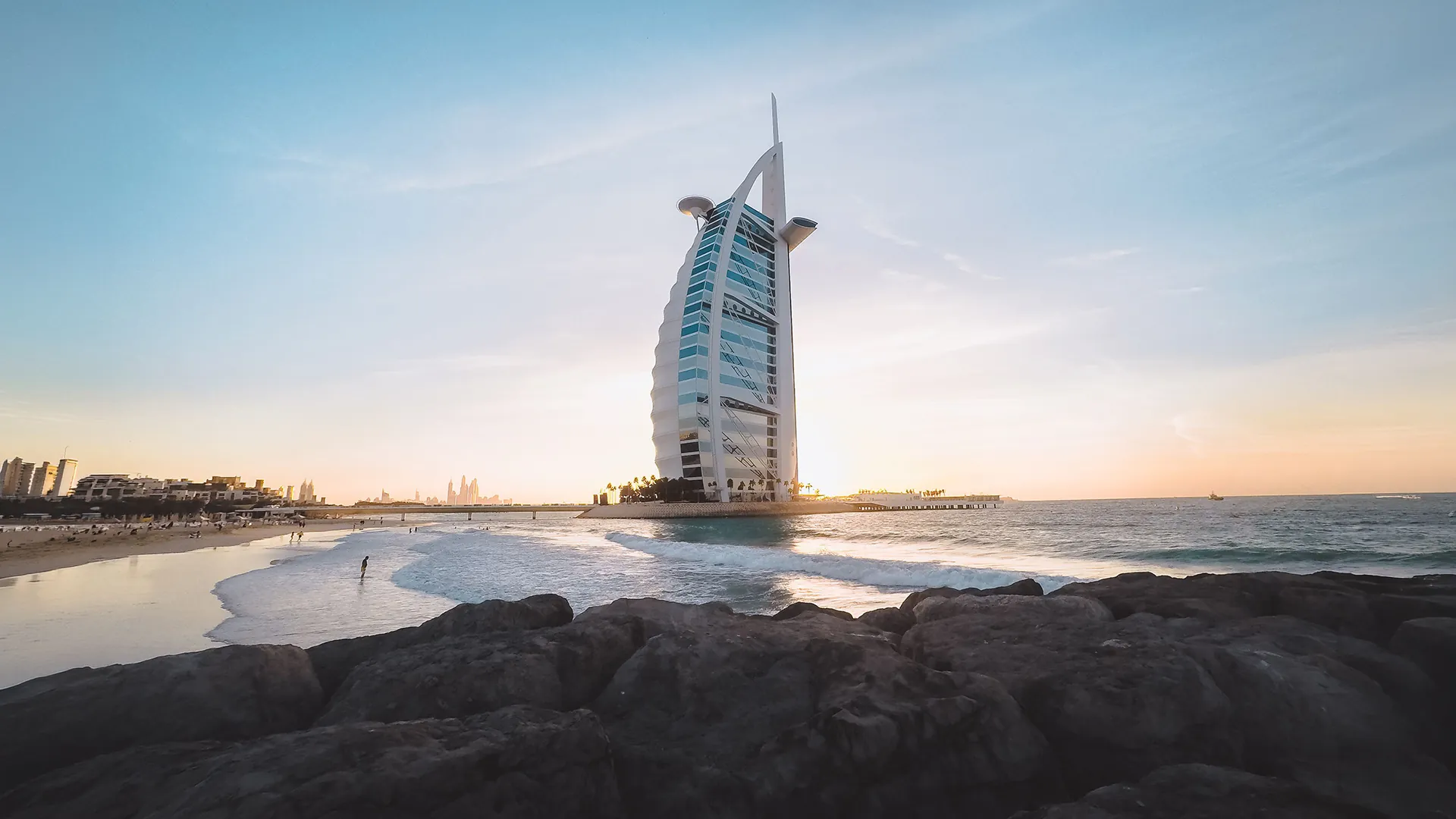 Burj Al Arab rising above Jumeirah Beach at sunset, seen from the rocky shoreline