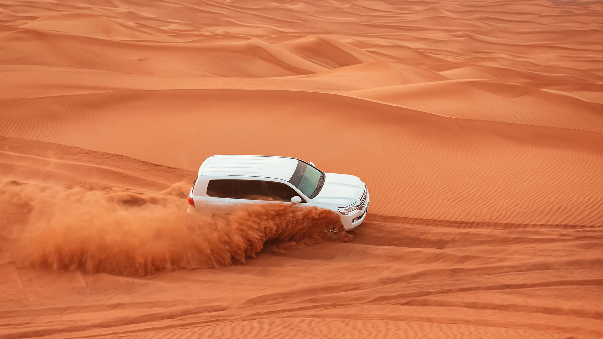 White 4x4 dune bashing through red sand on a Dubai desert safari