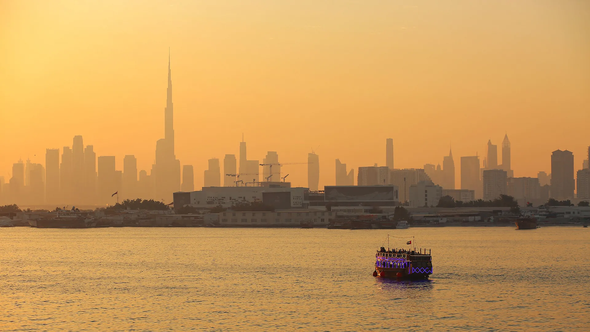 Illuminated dhow on the water with the Dubai skyline and Burj Khalifa in golden haze