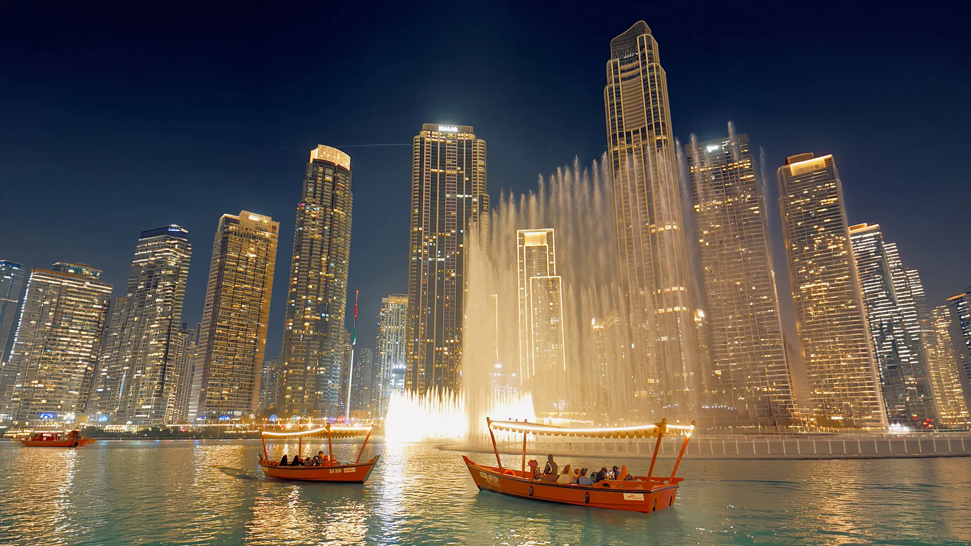 Abra boats on the lake beside the Dubai Fountain and lit-up Downtown towers at night