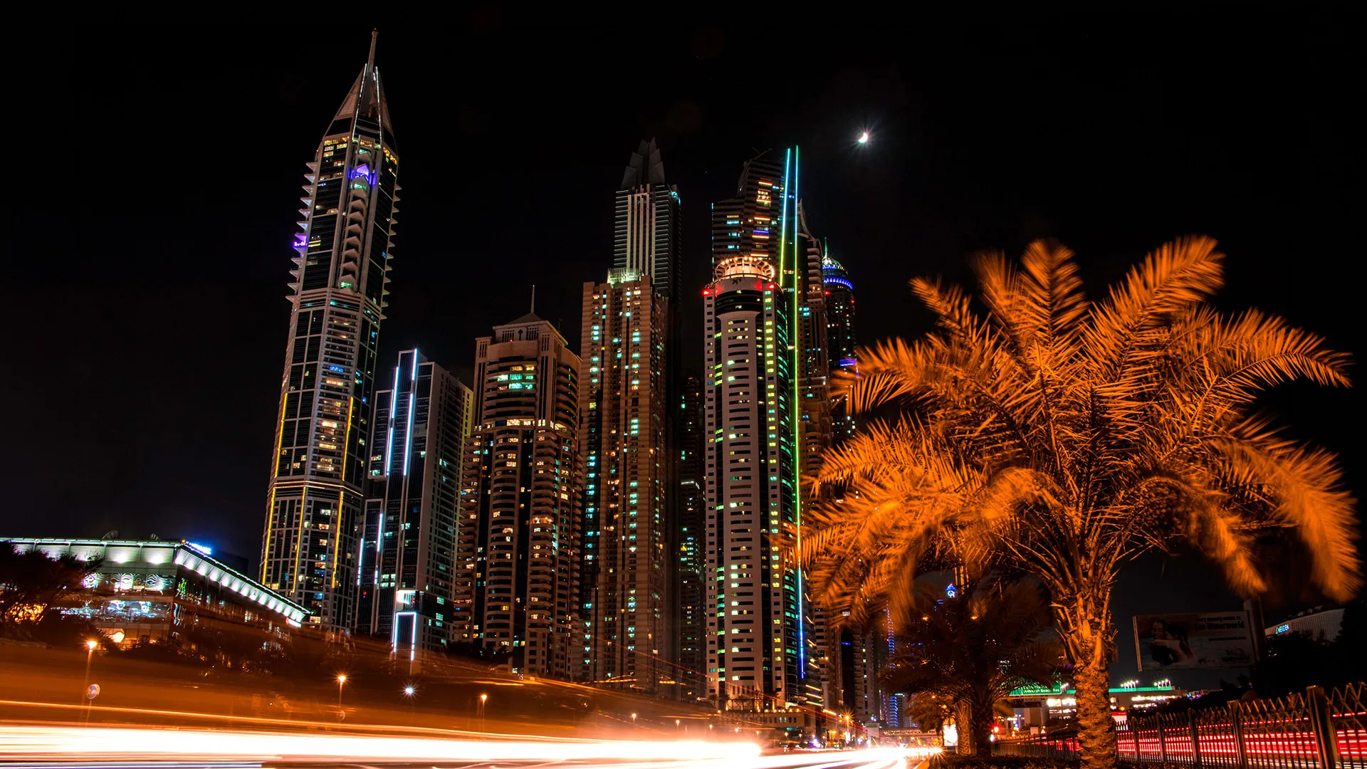 Dubai Marina towers lit up at night beside glowing palm trees and light trails
