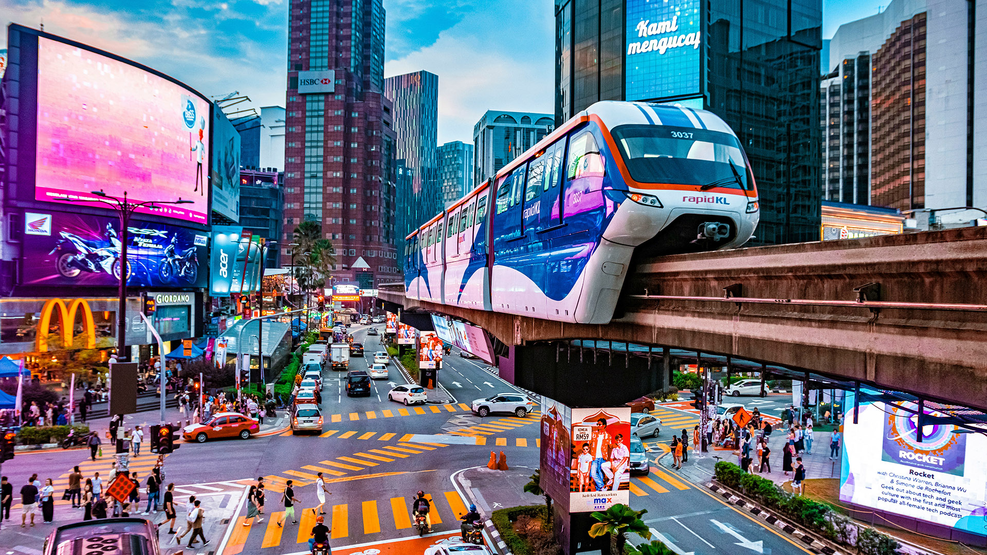 Kuala Lumpur city intersection with a monorail train, traffic, and glowing billboards