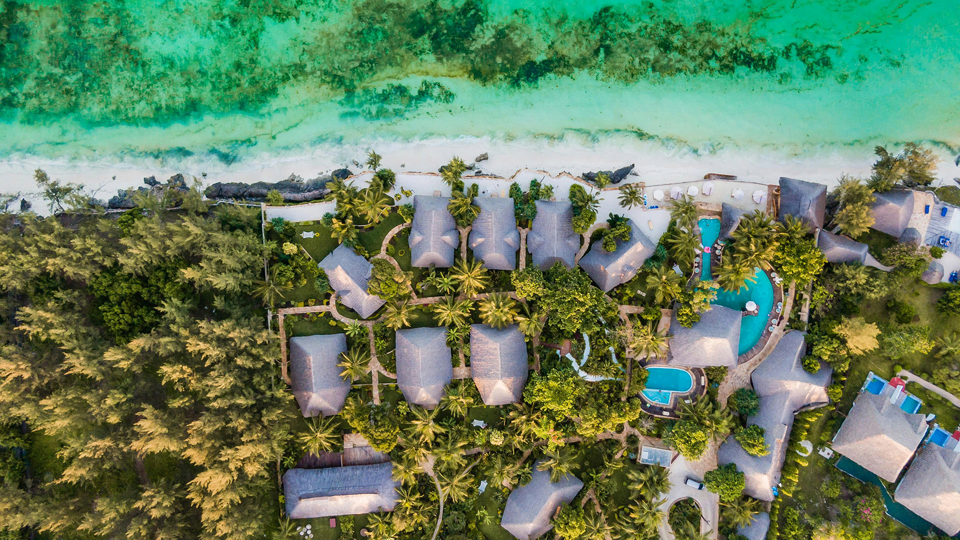 Bird's-eye view of a beachfront resort with pools beside turquoise Zanzibar waters