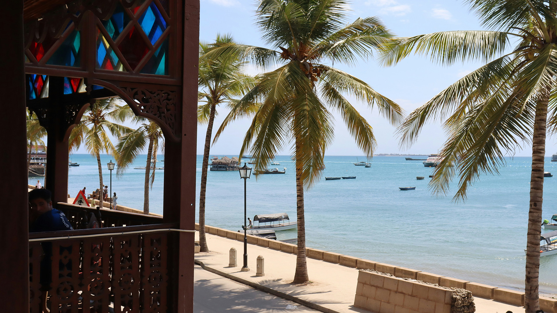 Stone Town balcony with stained glass overlooking palms and boats on the Indian Ocean