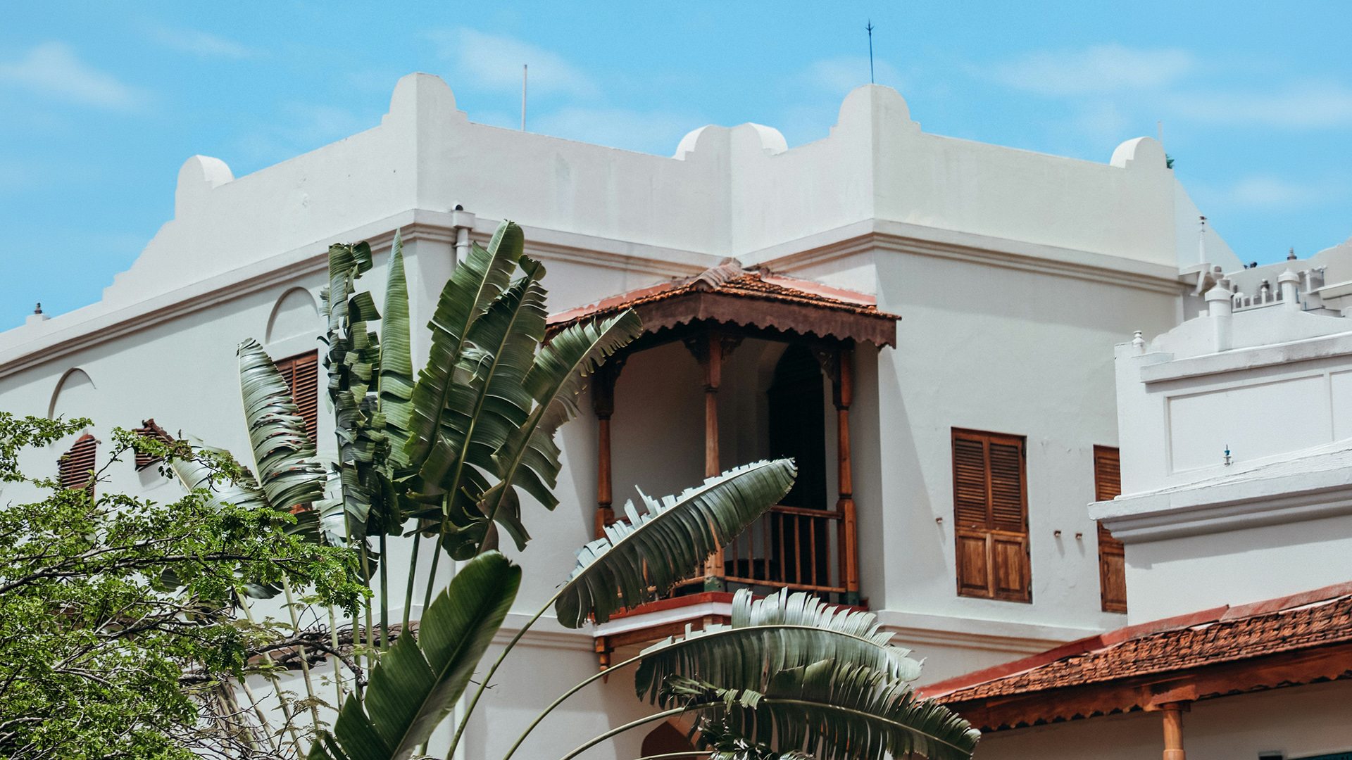 White colonial Stone Town building with wooden shutters framed by tropical foliage